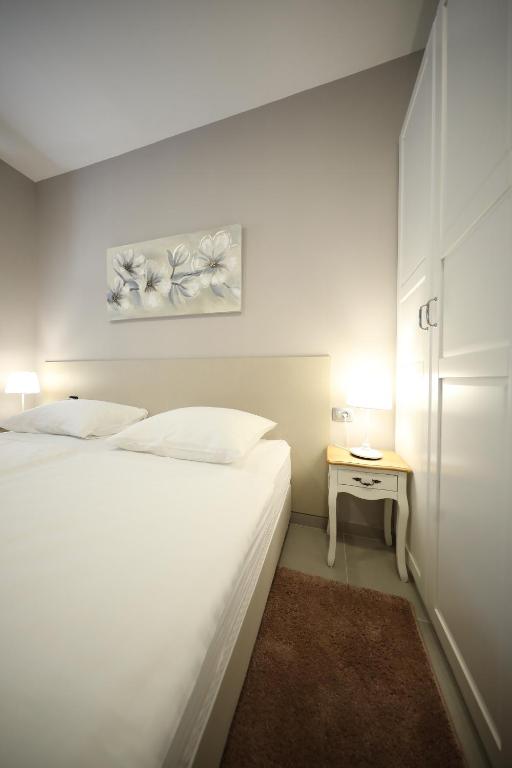 a white bedroom with a bed and a small table at Teatro Verdi Accommodation in Zadar