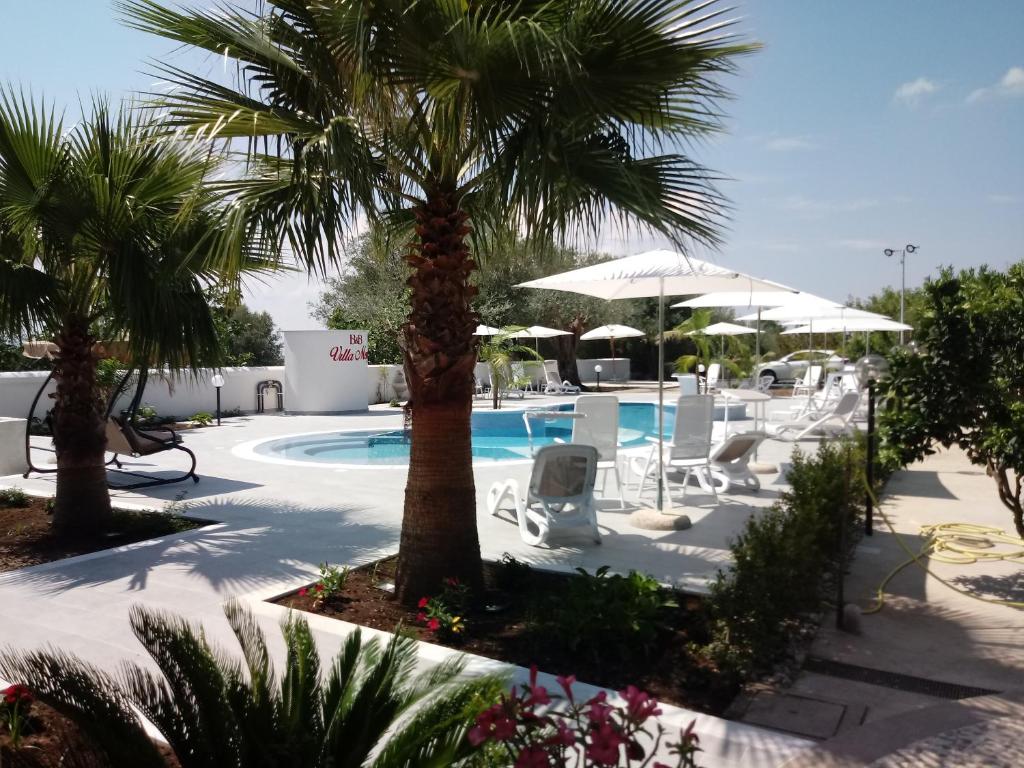 a resort with a pool and palm trees and chairs at B&B Villa Mery in Mileto