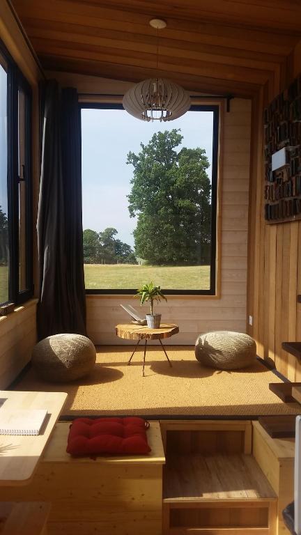 a room with a large window with a table and pillows at La Tiny du Parc : Saint Symphorien des Monts in Saint-Symphorien-des-Monts