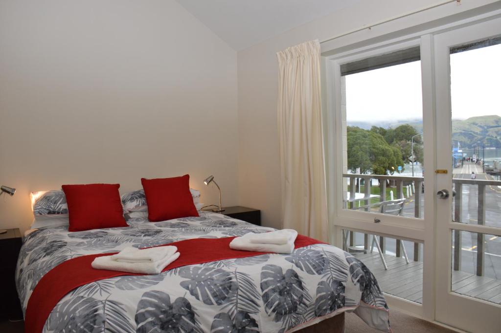 a bedroom with a bed with red pillows and a balcony at Akaroa Central Apartment in Akaroa