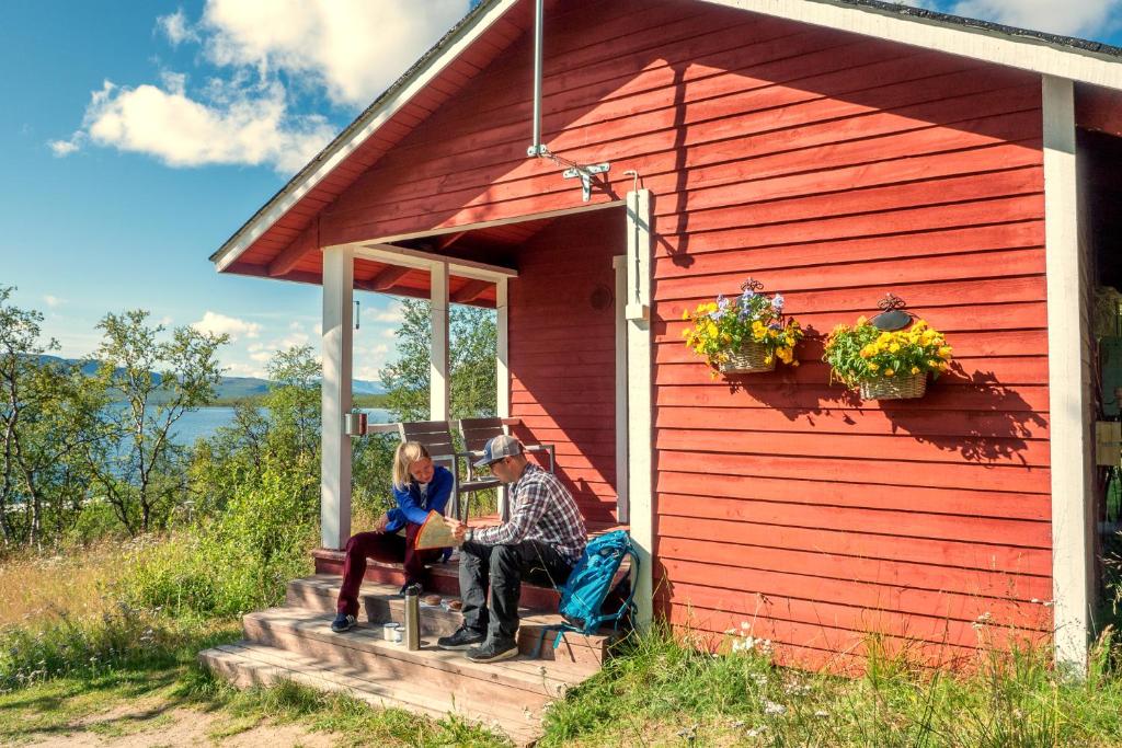 Due persone sedute sul portico di un capanno rosso di Kilpisjärven Retkeilykeskus Cottages a Kilpisjärvi