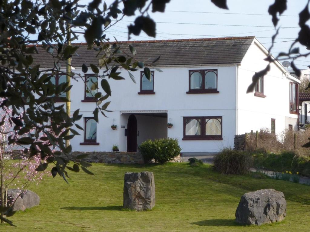 a white house with rocks in front of it at Banfield Lodge for Gower in Swansea