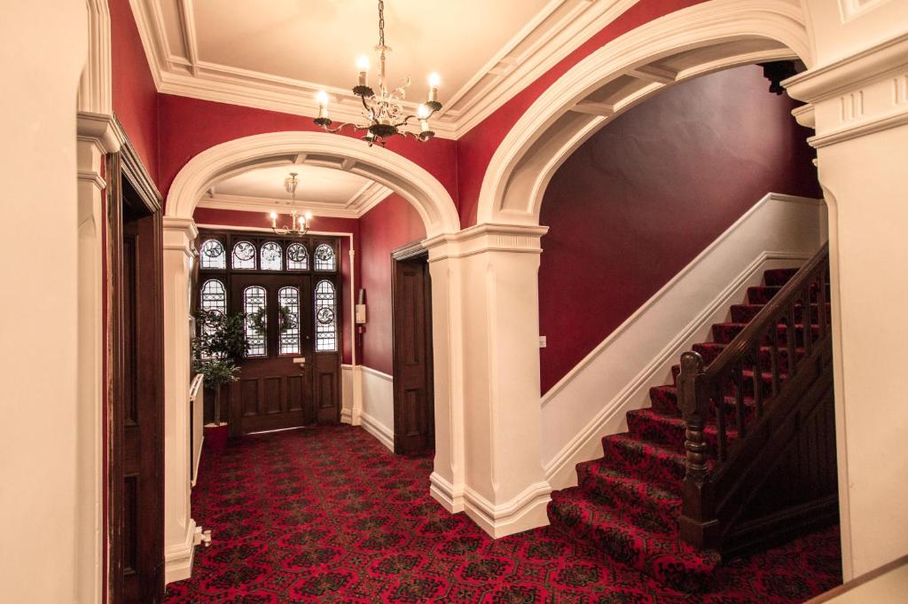 a hallway with red walls and stairs with a chandelier at Elim Bank Guest House in Bowness-on-Windermere