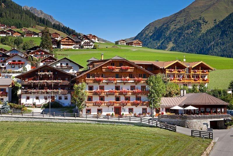 a large hotel with a green hill in the background at Hotel Hofmann in Santa Maddalena in Casies