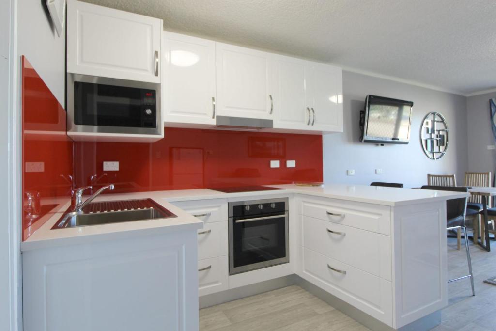 a kitchen with white cabinets and red walls at Beachfront 4, 25 Willow Street in Crescent Head