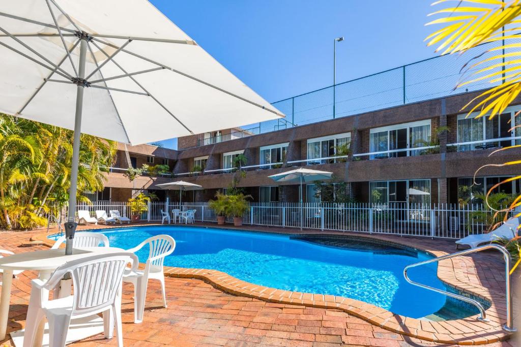 una piscina con sillas y una sombrilla y un edificio en Aquajet Motel, en Coffs Harbour