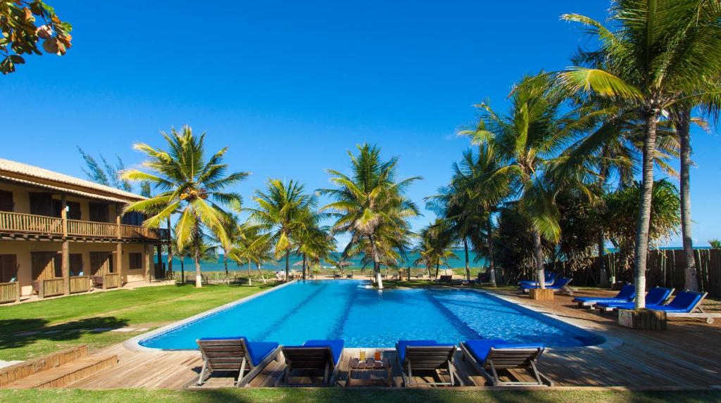 uma grande piscina com cadeiras e palmeiras em Pousada Praia das Ondas - Pé na areia em Itacimirim