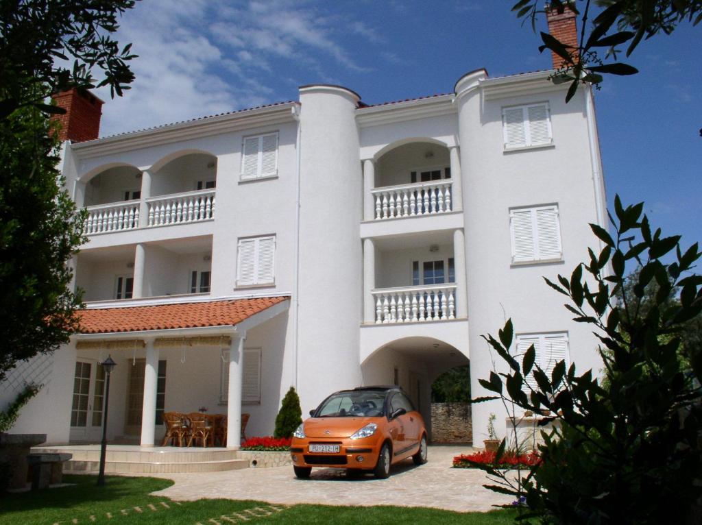 une voiture orange garée devant un bâtiment blanc dans l'établissement Apartments Paloma Blanca, à Medulin