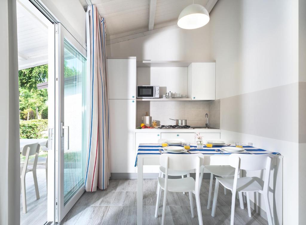 a white kitchen with a dining table and chairs at Villaggio San Francesco in Duna Verde