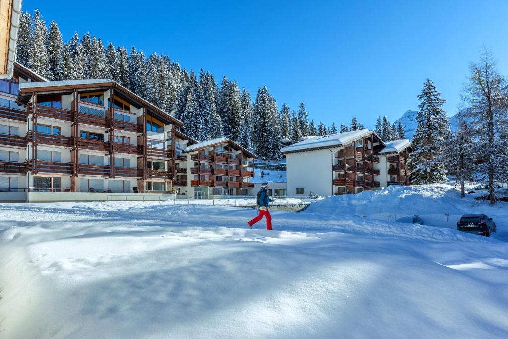 a person walking in the snow in front of a lodge at I dr Rehwiesa B02 in Arosa