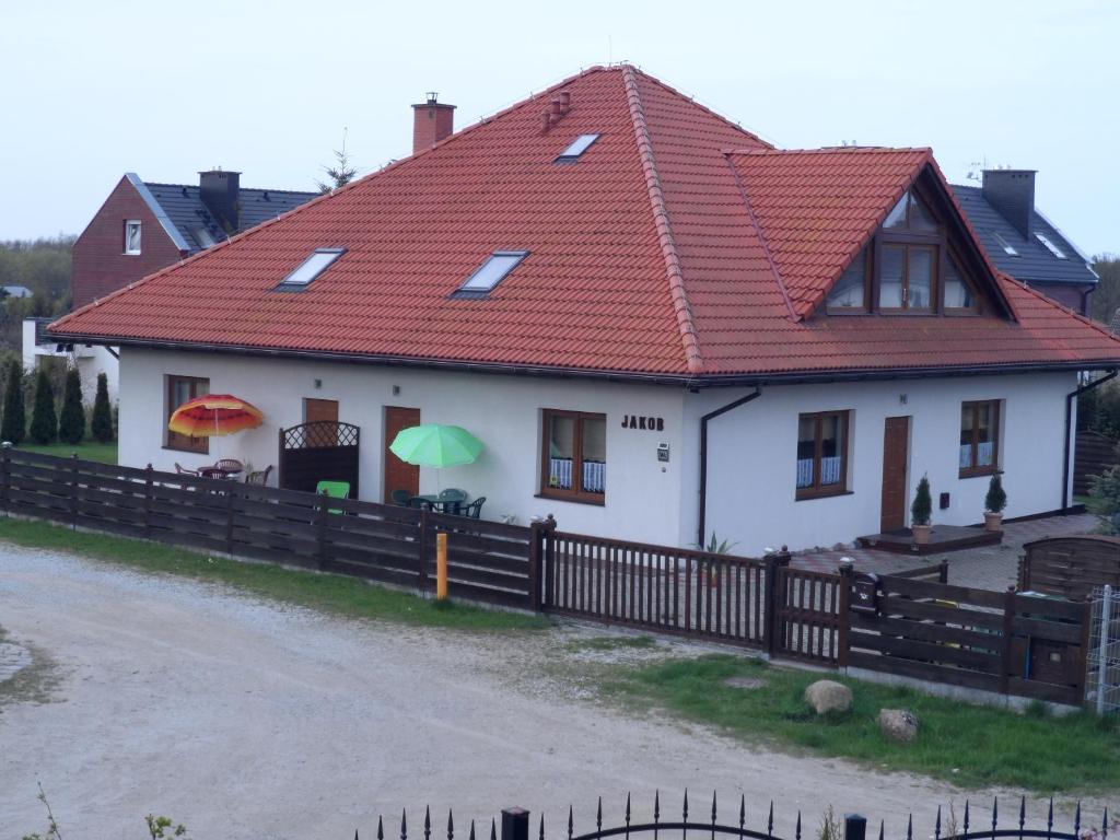 a white house with a red roof and a fence at Apartamenty Jakob in Rewal