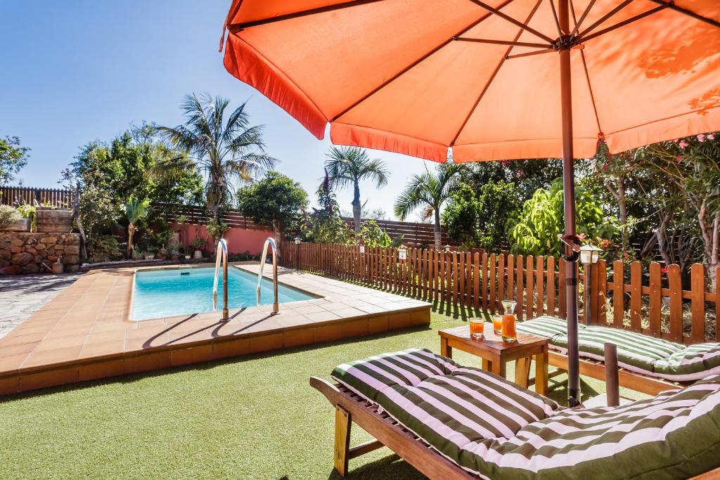 a pool with two chairs and an orange umbrella at El Tendal in Puntagorda