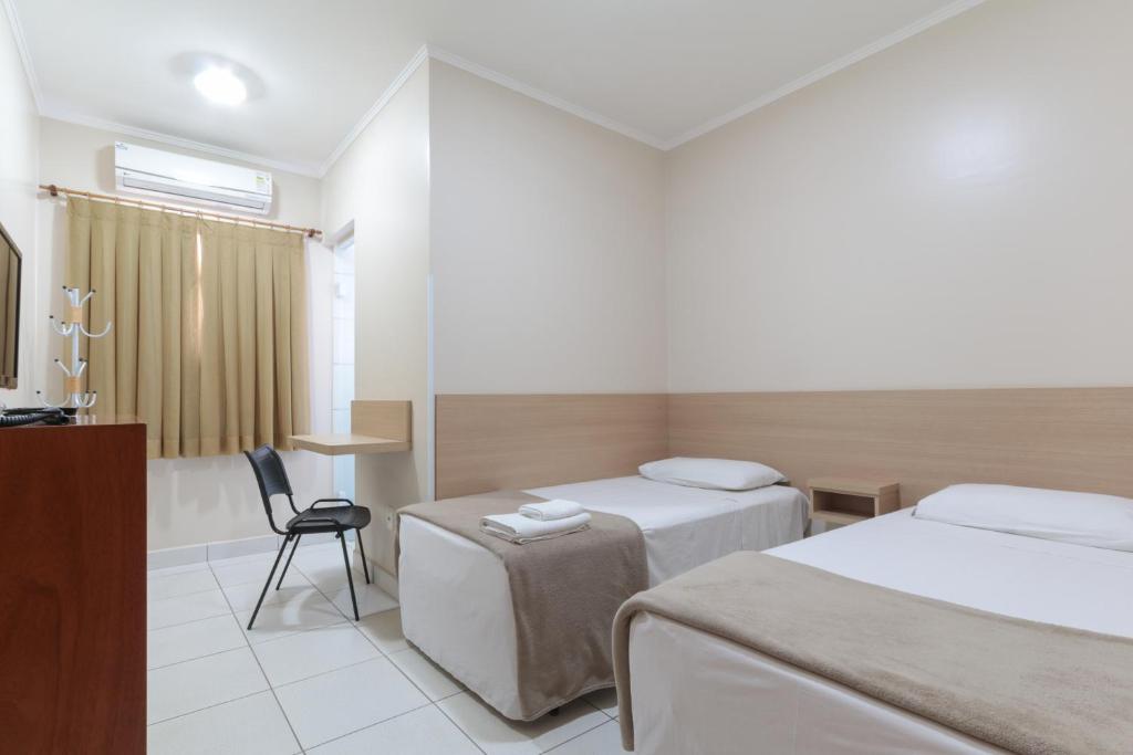 a hotel room with two beds and a desk at Hotel Copacabana Piracicaba in Piracicaba