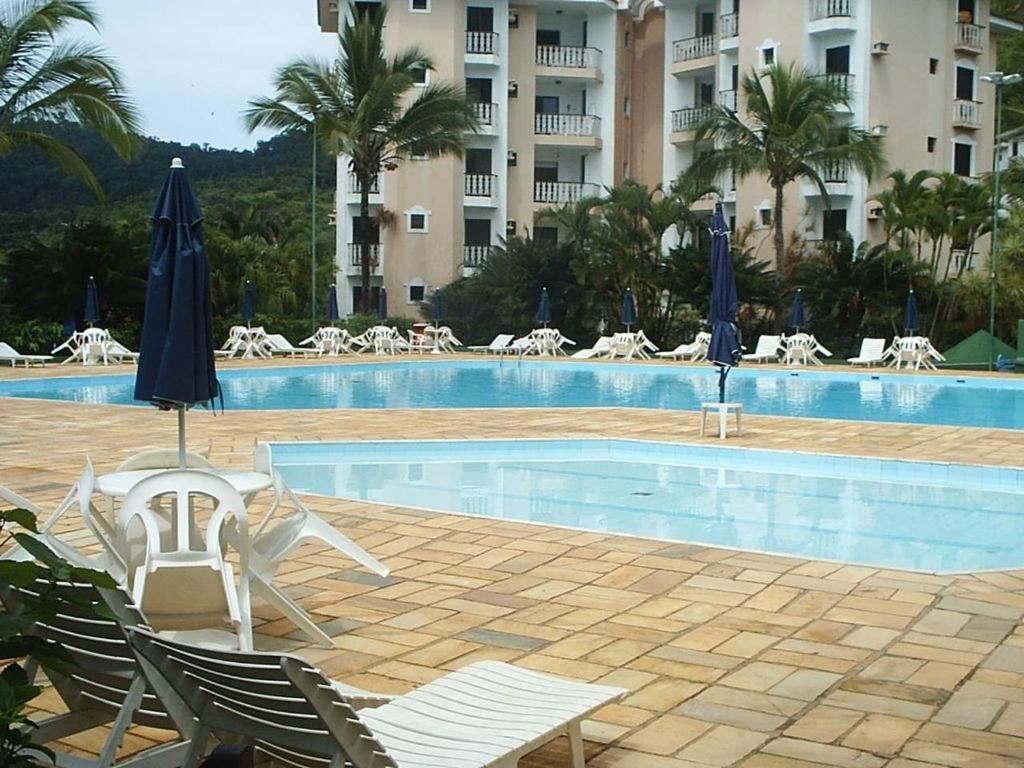 a swimming pool with chairs and umbrellas next to a hotel at Apartamento Condomínio Wembley Tênis - Toninhas - Ubatuba - SP in Ubatuba