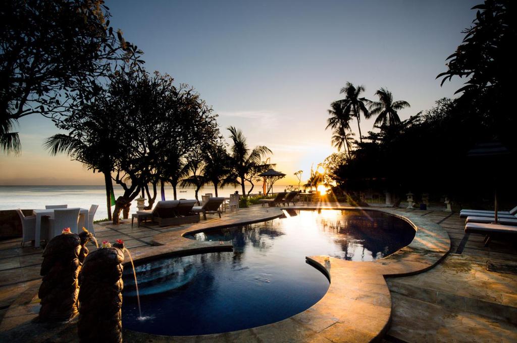 una piscina en un complejo con palmeras y el océano en Poinciana Resort, en Tejakula