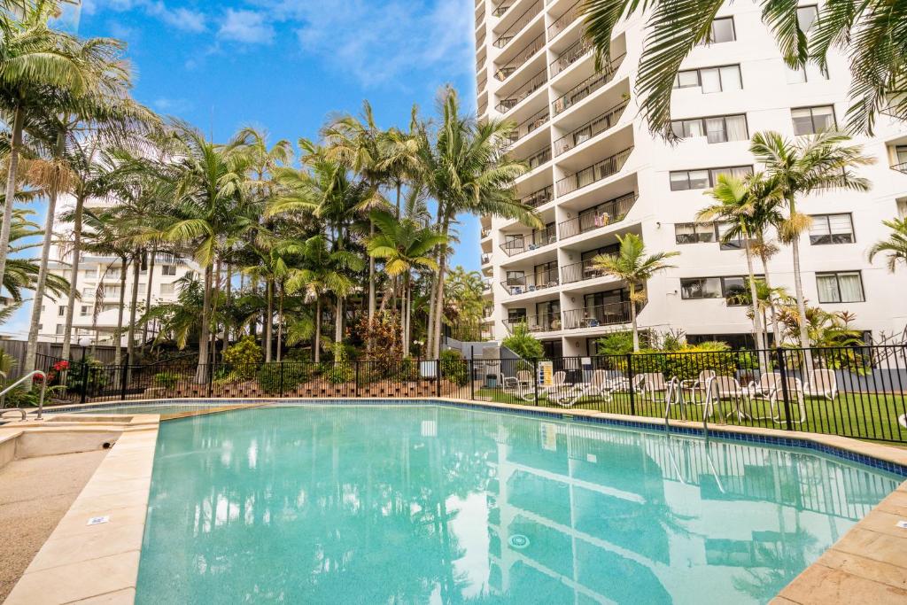 a swimming pool with palm trees in front of a building at Horizons Holiday Apartments - OFFICIAL in Gold Coast