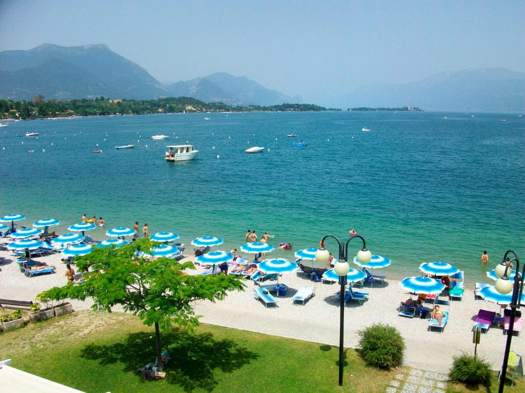 a beach with blue umbrellas and people in the water at Hotel La Romantica in Manerba del Garda
