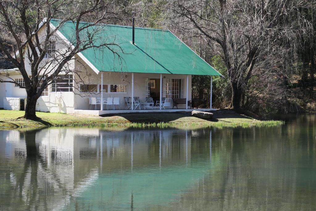 une maison avec un toit vert à côté d'une masse d'eau dans l'établissement Mkomazana Mountain Cottages, à Himeville
