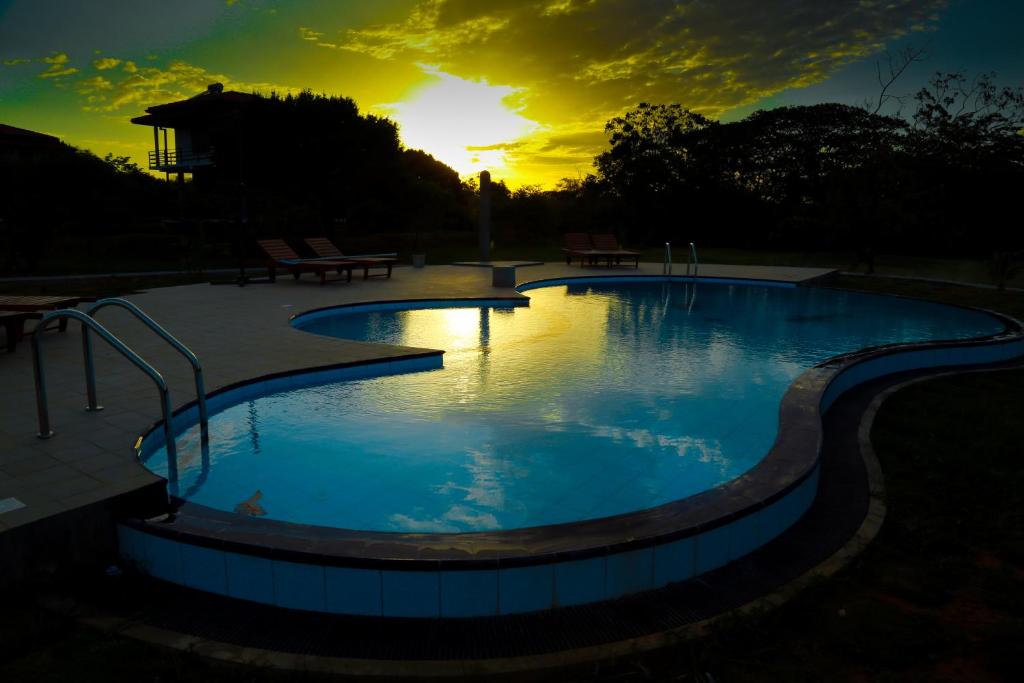 a large swimming pool with a sunset in the background at Lake Villa Resort in Tissamaharama