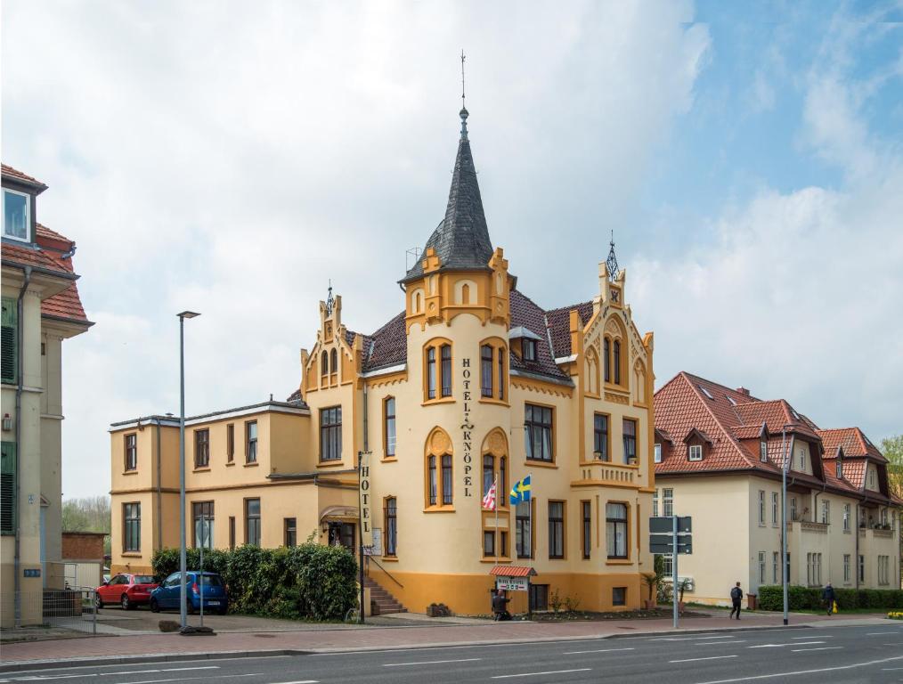 ein großes gelbes Gebäude mit einem Turm auf einer Straße in der Unterkunft Hotel Knöpel in Wismar