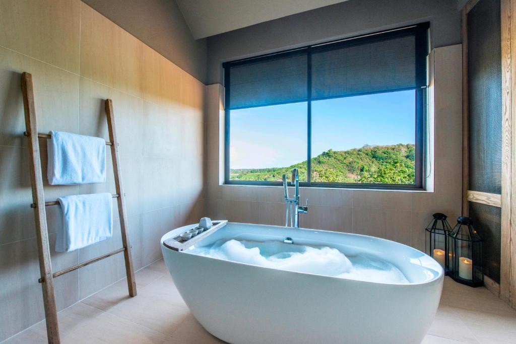 a bath tub in a bathroom with a large window at Sunsuri Phuket - SHA Plus in Nai Harn Beach