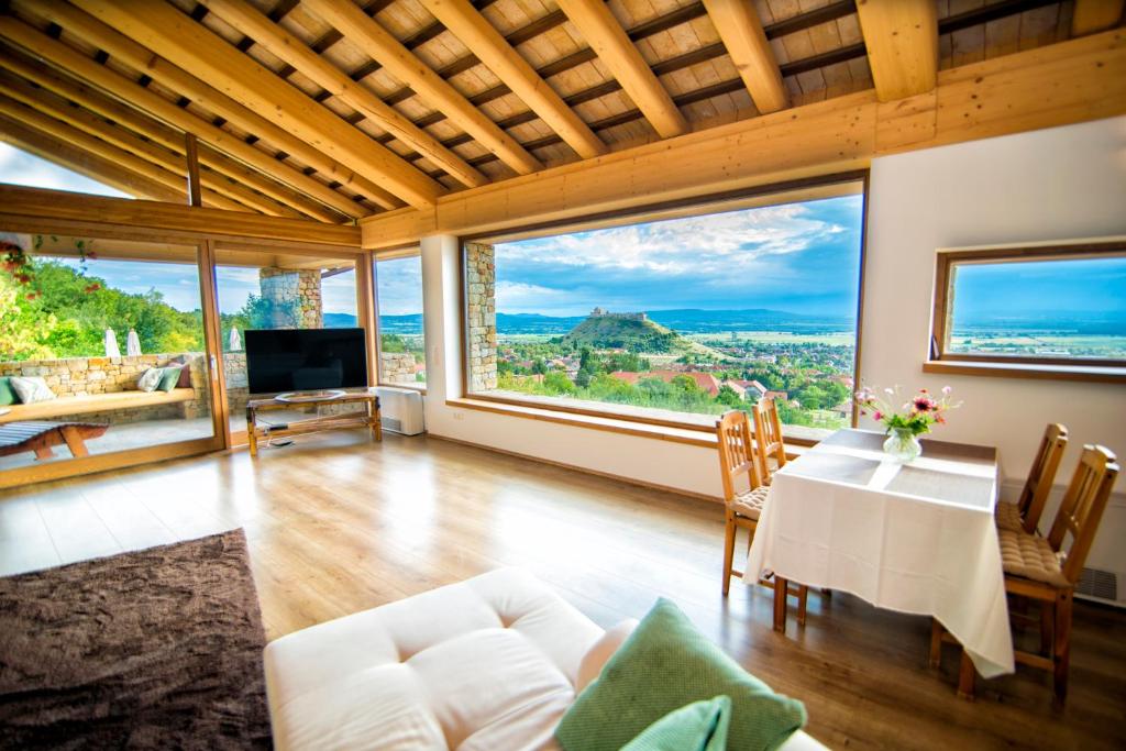 ein Wohnzimmer mit einem Tisch und Stühlen sowie großen Fenstern in der Unterkunft Villa Terazza-Panorama Apartman in Sümeg