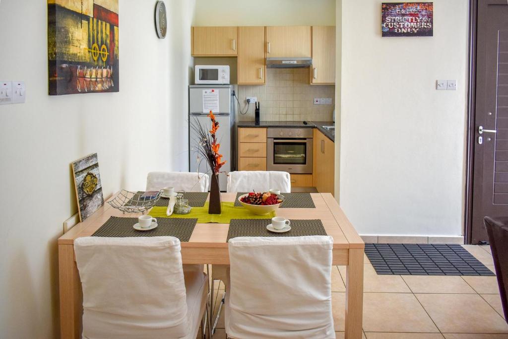 una cocina con mesa de madera con sillas blancas y mesa en Amigos Apartment Mythical en Protaras