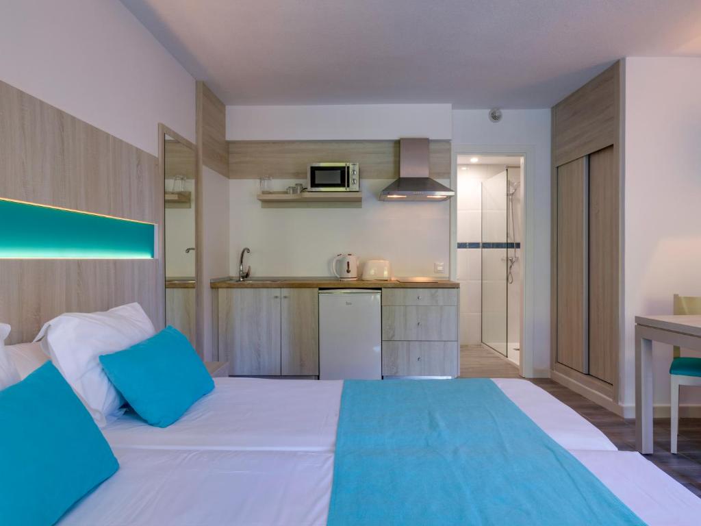 a bedroom with a large white bed and a kitchen at Comitas Floramar in Cala Galdana