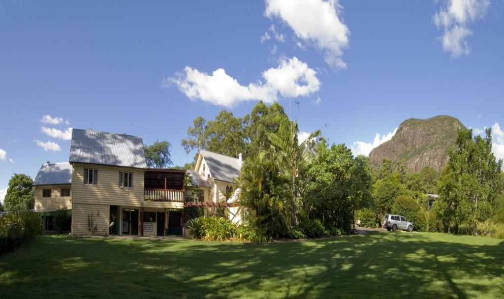 uma casa num relvado com montanhas ao fundo em Glass House Mountains Ecolodge em Glass House Mountains