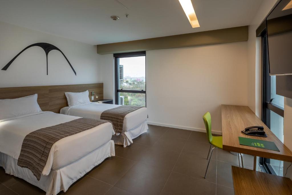 a hotel room with two beds and a table and a desk at Linx Galeão in Rio de Janeiro