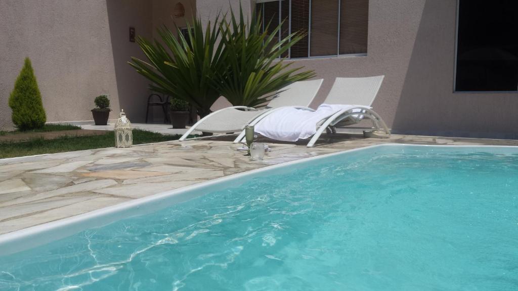 einen Pool mit zwei Gartenstühlen und einem Pool in der Unterkunft Casa Caraguatatuba com Piscina e Wifi in Caraguatatuba