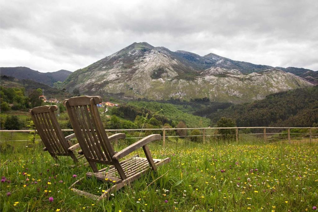 two chairs sitting in a field with a mountain at Hotel El Babú in Caravia