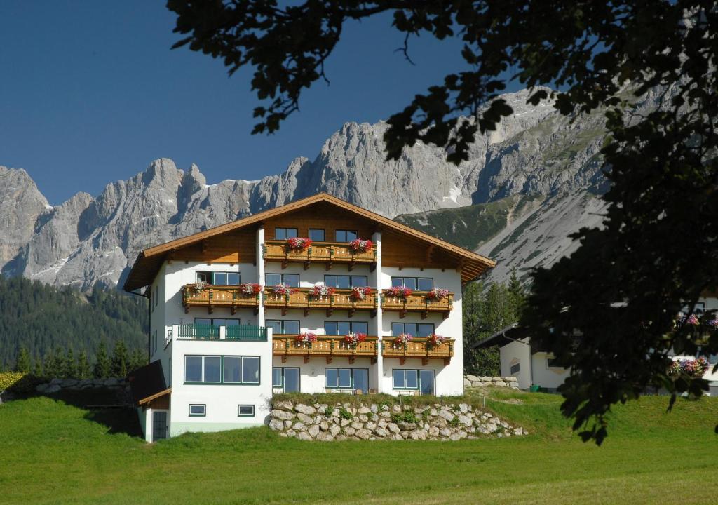 a building with flowers on the balconies in front of mountains at Aparthotel Sunrise in Ramsau am Dachstein