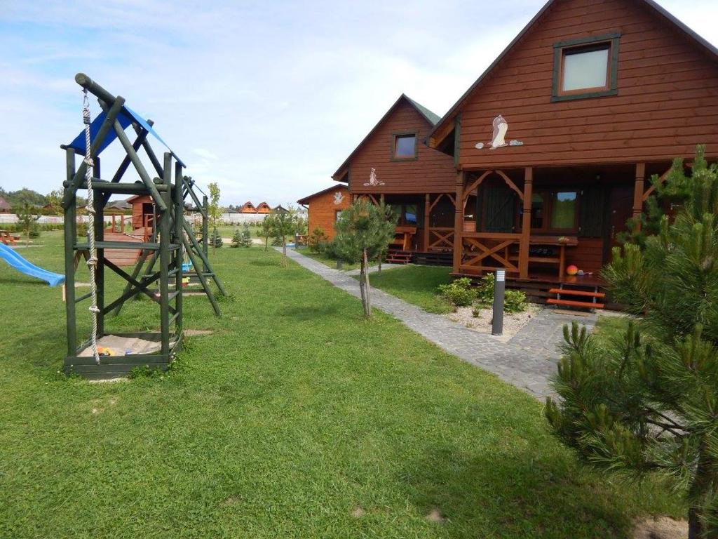Playground swing set on left, cobblestone path leading past wooden cabins on sunny day.