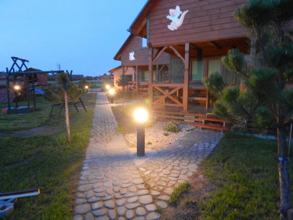 Evening cobblestone path lit by round bollard lights, wooden cabins glowing warmly.
