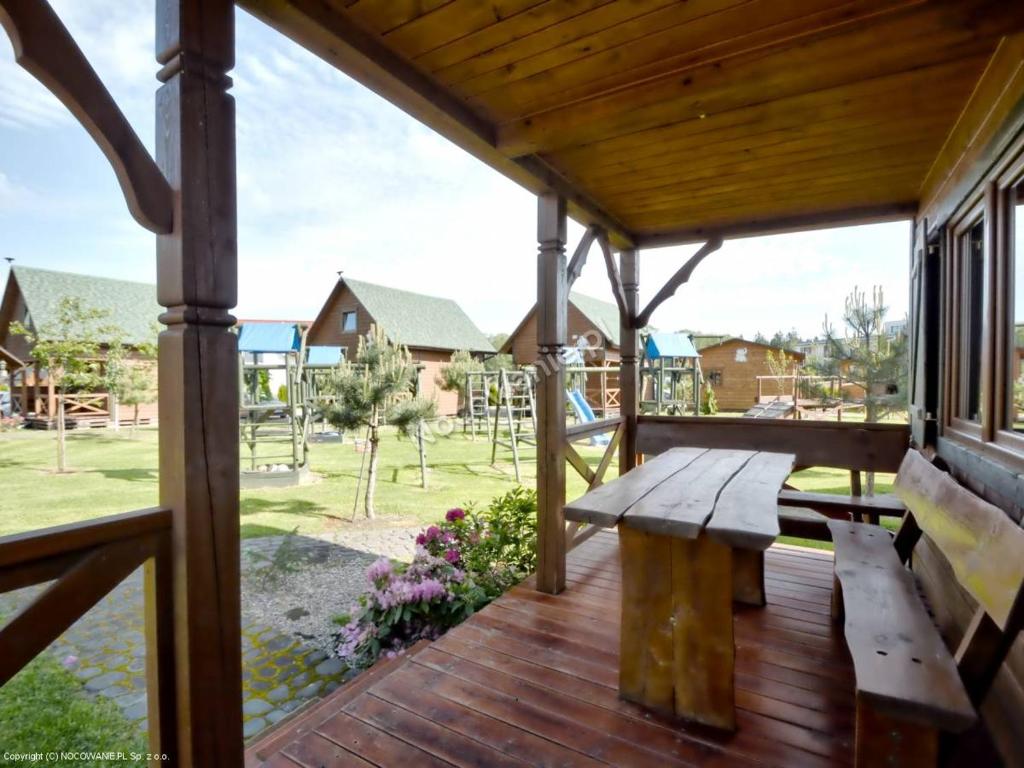Covered wooden porch with rustic bench and table overlooking playground and neighboring cabins.
