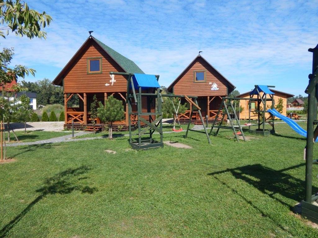 Children's playground with swings and slide in front of two wooden cabins, sunny.