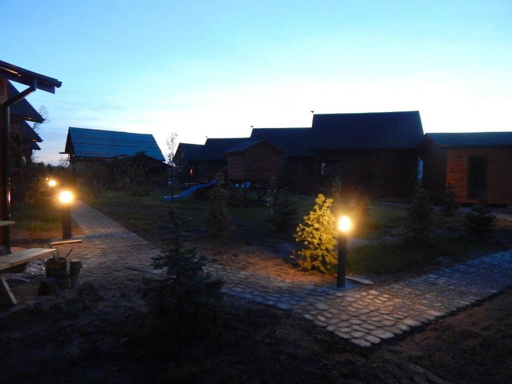 Dusk scene with glowing pathway lamps, silhouetted wooden cabins and quiet playground.