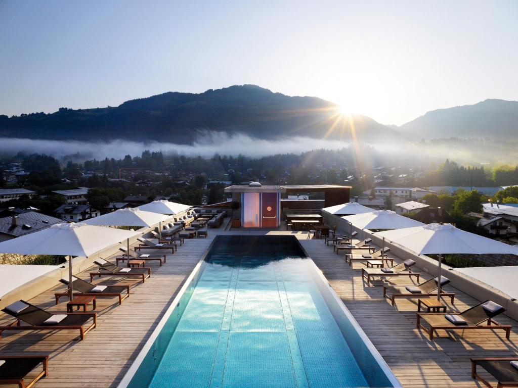 a resort with a swimming pool and chairs and the sun at Schwarzer Adler Kitzbühel - Adults Only in Kitzbühel