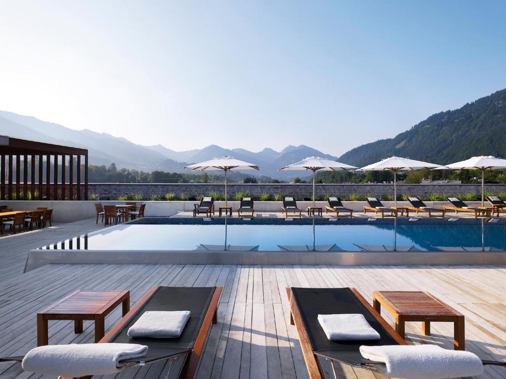 a resort with a swimming pool and mountains in the background at Schwarzer Adler Kitzbühel - Adults Only in Kitzbühel