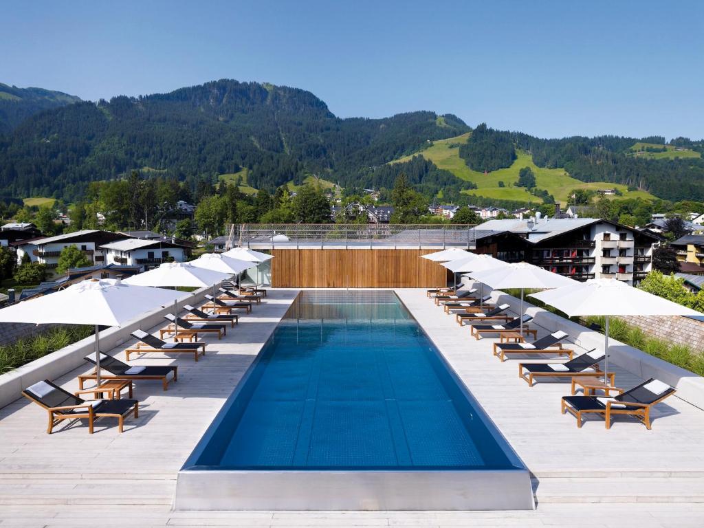 a swimming pool with lounge chairs and umbrellas at Schwarzer Adler Kitzbühel - Adults Only in Kitzbühel