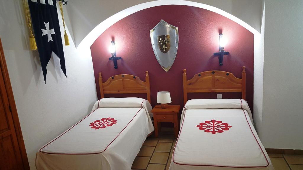 two beds in a room with two lights on the wall at Hotel Rural Hospedería de los Calatravos in La Calzada de Calatrava