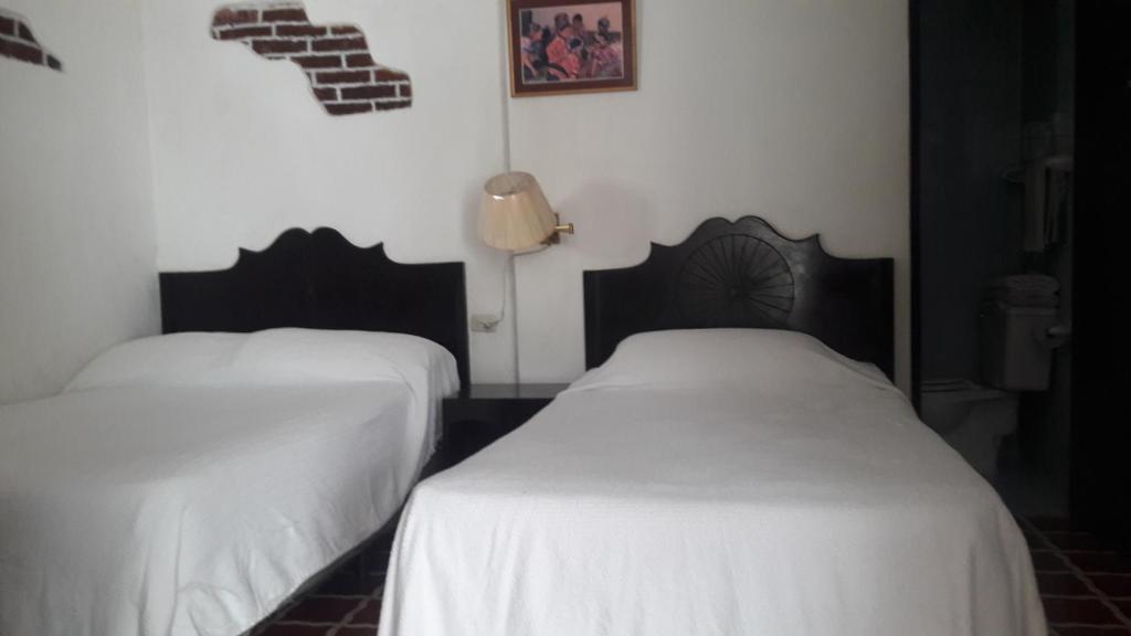 two beds in a room with white sheets at Hotel De Cortez y Larraz in Antigua Guatemala