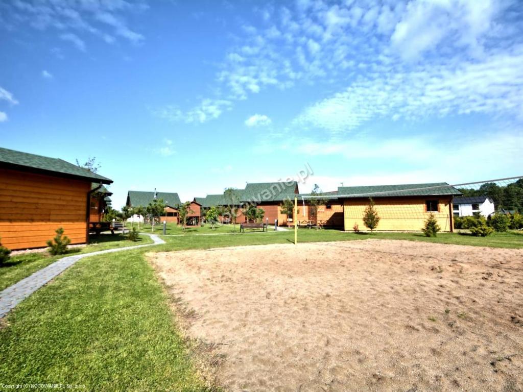 Sandy volleyball court foreground, green lawn and multiple wooden cabins under bright blue sky.