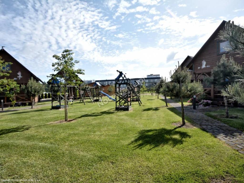 Green courtyard with multiple playground structures, young trees and row of wooden cabins.
