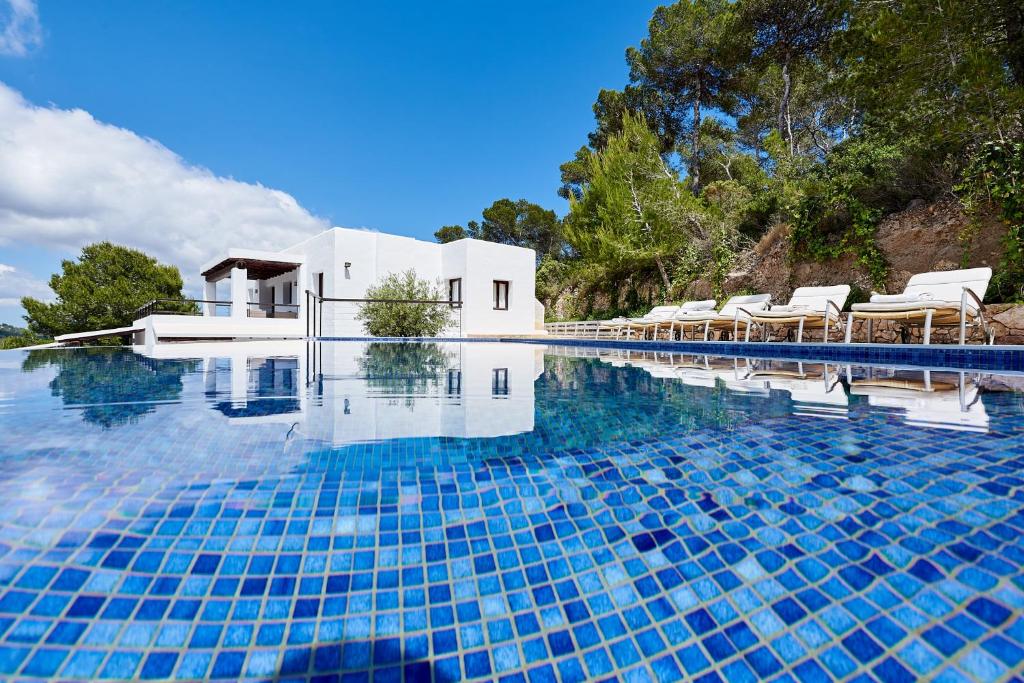 a swimming pool with chairs and a house at Villa Can Kiva in Es Cubells