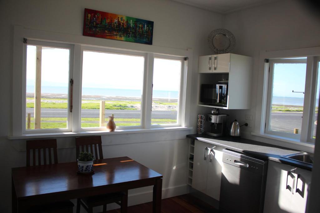 a kitchen with two windows and a table with a tableablish at Sea Urchin Cottage in Miranda