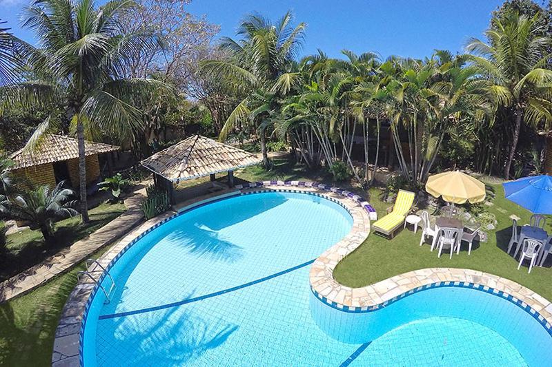 a large swimming pool with tables and chairs and palm trees at Eurosol Pousada das Canoas in Pipa