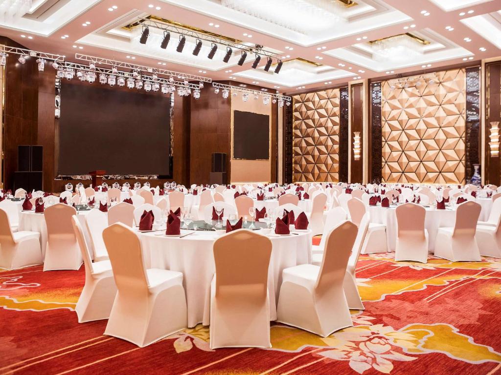 a banquet hall with white tables and chairs and a screen at Novotel Daqing Haofang in Daqing