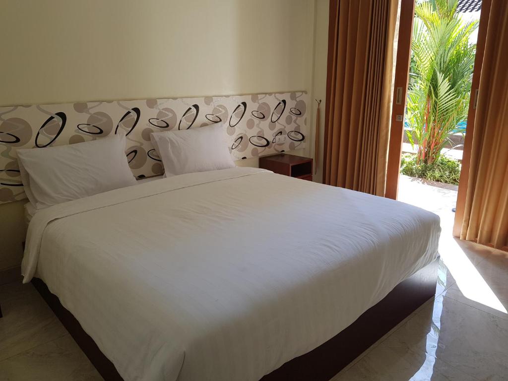 a bedroom with a large white bed and a window at Praba Guesthouse in Kuta